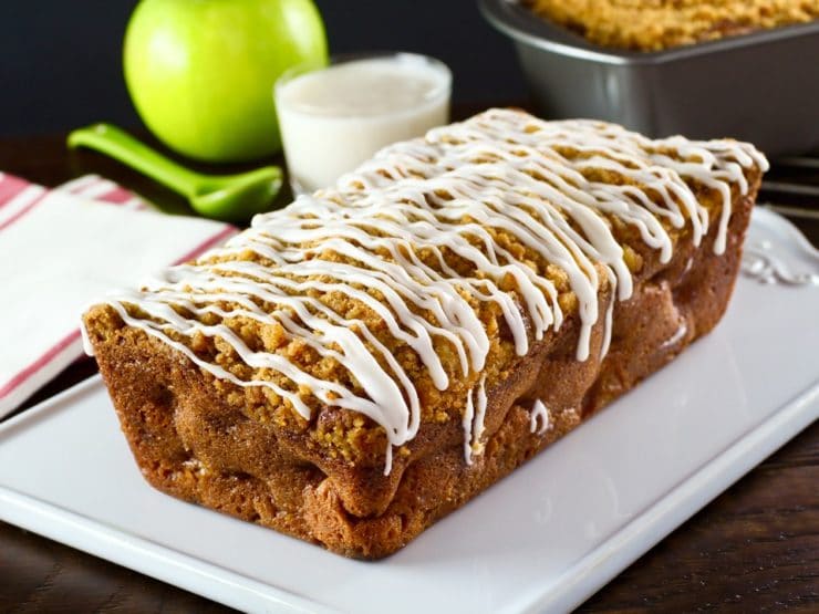 Greek Yogurt Apple Streusel Cake unsliced on white plate with cloth napkins, dish of yogurt, spook and green apple in background.