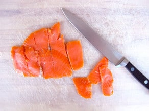 Slicing smoked salmon on a cutting board.