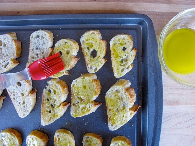 Brushing sliced baguette with olive oil.