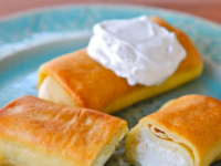 Three Ratner's Cheese Blintzes on a blue plate, topped with a generous dollop of whipped cream