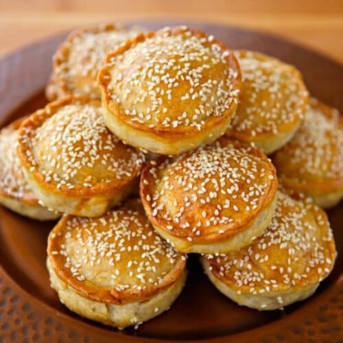 Sephardic Meat Hand Pies sprinkled with sesame seeds stock on top of each other served in a fancy brown plate