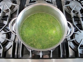 Broccoli stirred into broth in stockpot.