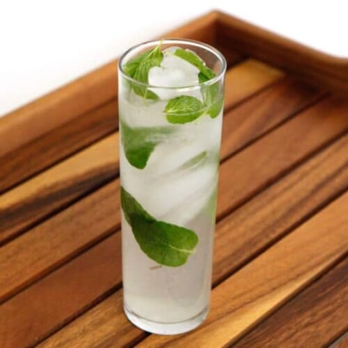 A tall glass of Mojito cocktail with mint leaves served on a wooden tray