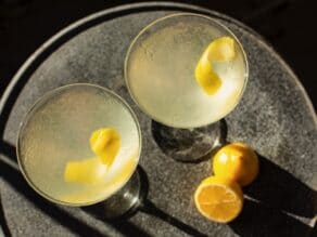 Horizontal overhead shot of two martini glasses filled with a lemon vanilla vodka cocktail garnished with a lemon peel twist.
