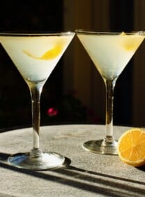 Horizontal shot of two martini glasses filled with a lemon vanilla vodka drink garnished with a lemon peel twist.