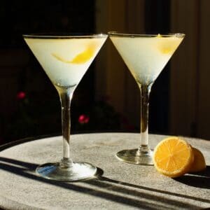 Horizontal shot of two martini glasses filled with a lemon vanilla vodka drink garnished with a lemon peel twist.