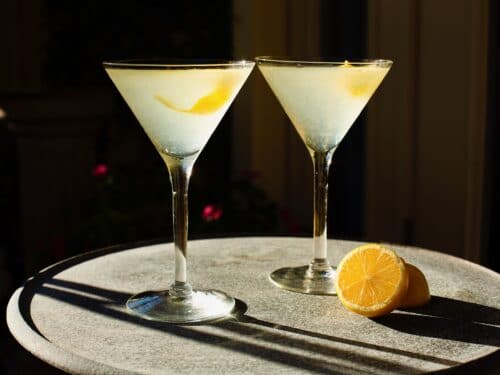 Horizontal shot of two martini glasses filled with a lemon vanilla vodka drink garnished with a lemon peel twist.