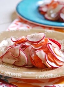 A plate of sliced radish and carrot salad on a plate and vibrant tablecloth