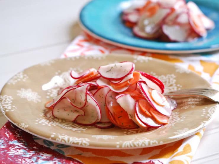 A plate of sliced radish and carrot salad on a plate and vibrant tablecloth