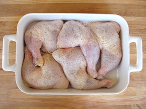 Chicken quarters in a greased baking dish.