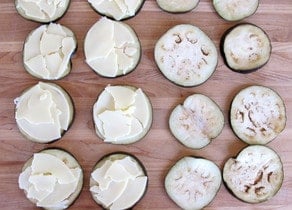 Adding sliced provolone on top of eggplant rounds.