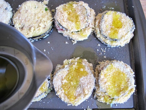 Drizzling oil over breaded eggplant.