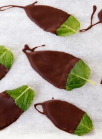 Chocolate dipped mint leaves on a parchment lined sheet.
