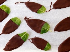 Chocolate dipped mint leaves on a parchment lined sheet.