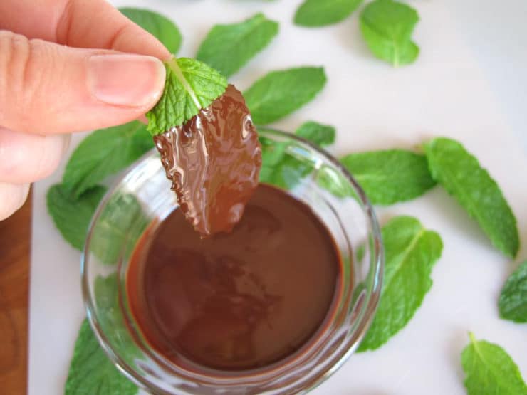 Dipping mint leaves in melted chocolate.