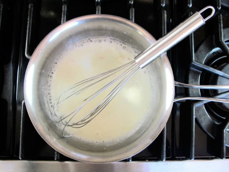Whisking milk into a roux in a saucepan.