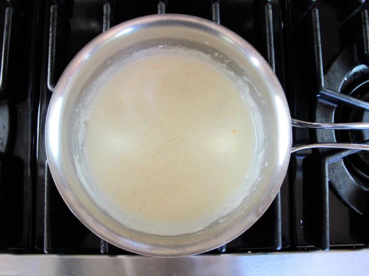 Goat cheese stirred into white sauce in a saucepan.