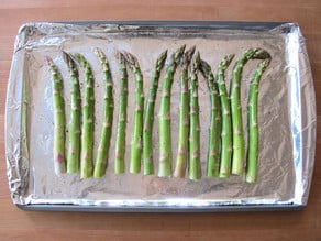 Asparagus stalks on a foil-lined baking sheet.
