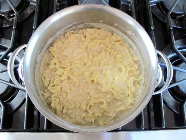 Egg blend mixed into cooked noodles in stockpot.