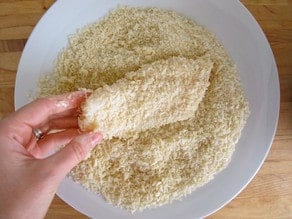 A hand breading a fish on breadcrumbs for Crispy Panko Fish