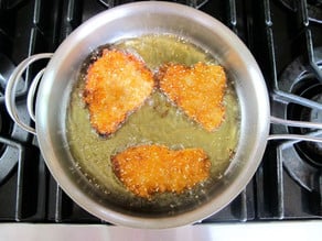 Coated fish fillets frying in a skillet.