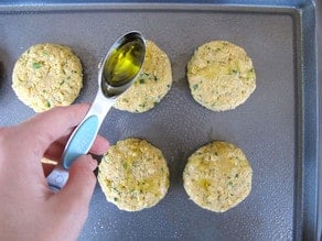 Drizzling oil over chickpea patties on a baking sheet.