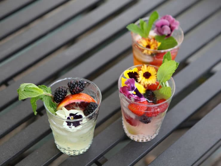 Three shot glasses filled with drinks and topped with berries, mint, and beautiful small flowers