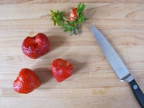 Hulled strawberries on a cutting board.