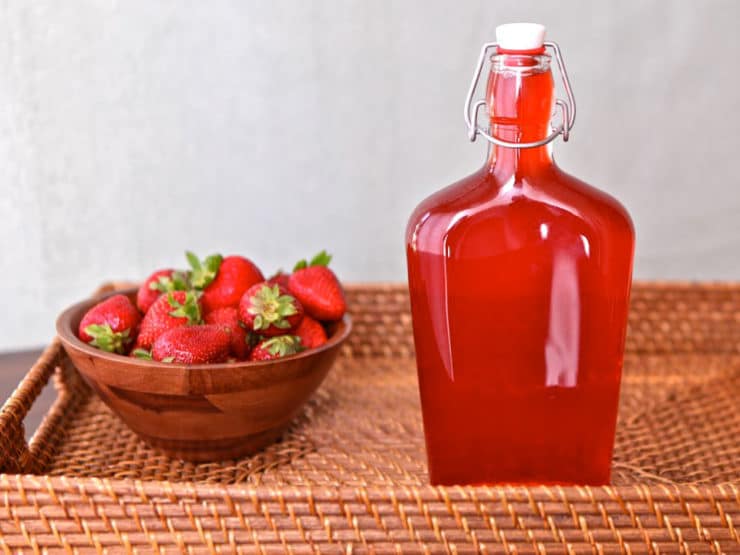 Strawberry jar next to a bowl of fresh strawberries inside a rectangular basket.