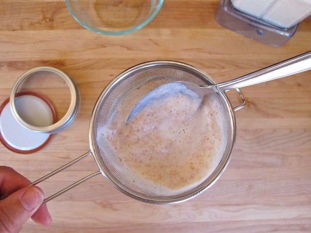Pushing all milk through the almond solids in a strainer.