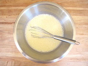 Milk whisked into eggs in a mixing bowl.
