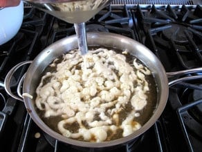 Drizzling funnel cake batter into hot oil.