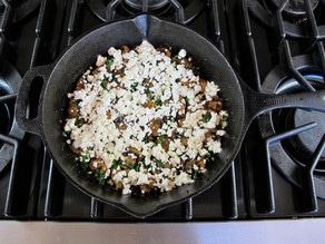Goat cheese sprinkled over mushrooms in a skillet.