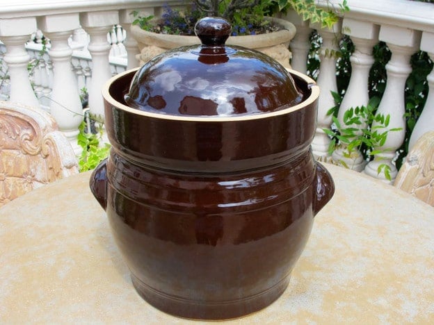 Brown ceramic fermentation crock on outdoor table.