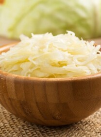 Bowl of fermented cabbage sauerkraut in wooden bowl with cabbage in background.