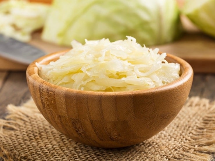 Bowl of fermented cabbage sauerkraut in wooden bowl with cabbage in background.