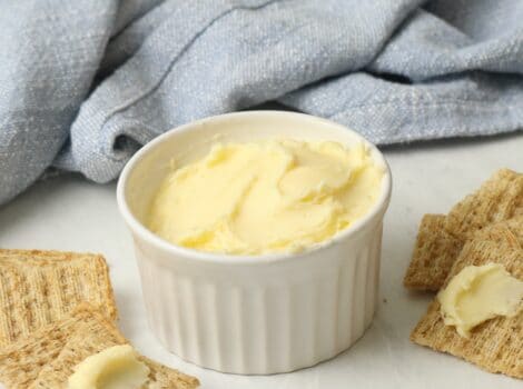 A dish of homemade butter on a marble surface, crackers spread with butter. Blue towel in background.