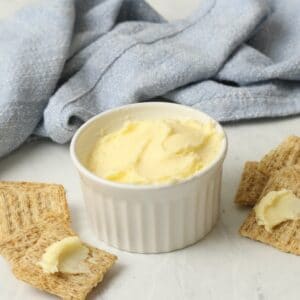 A dish of homemade butter on a marble surface, crackers spread with butter. Blue towel in background.