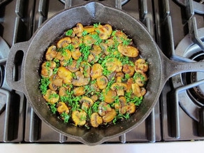 Herbs spread over sauteed mushrooms in a skillet.