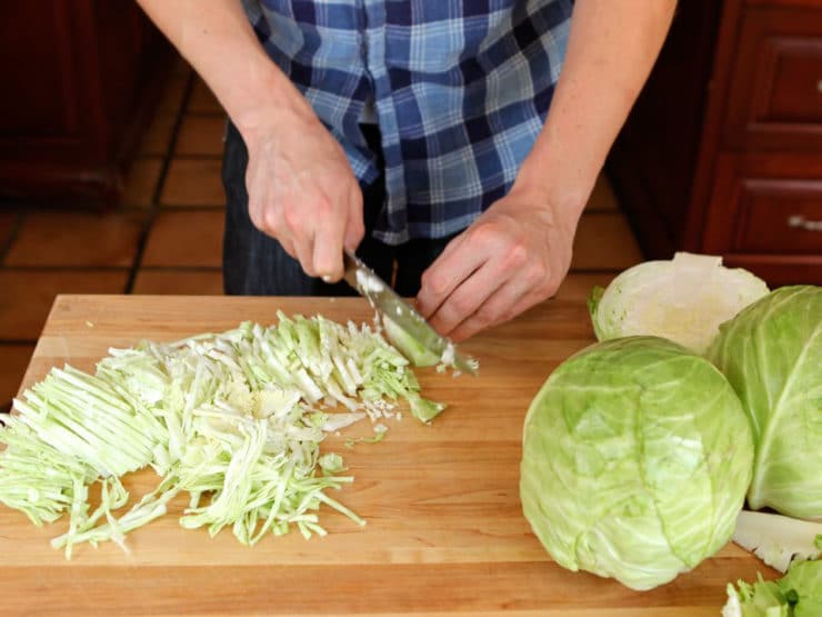 Male hands shredding cabbage on wooden cutting board.