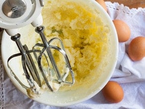Adding eggs to butter in a mixing bowl.
