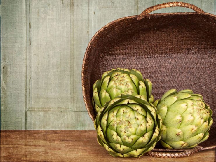 Artichokes beautifully arranged with a rustic brown basket in the background