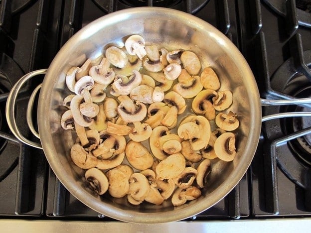 Sliced mushrooms frying in a saucepan.