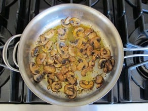 Sliced mushrooms frying in a saucepan.