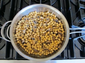 Chickpeas added to mushrooms in a saucepan.