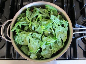 Spinach and kale added to a saucepan.