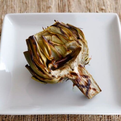 Grilled artichokes on a white square-shaped plate.