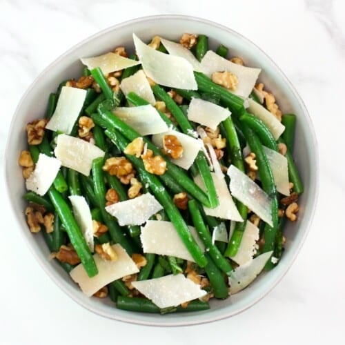 Green bean salad with walnuts and parmesan as garnish on a white bowl.