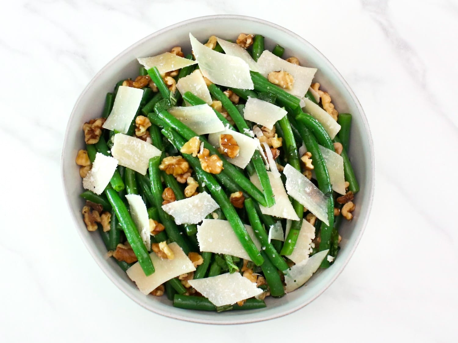 Green bean salad with walnuts and parmesan as garnish on a white bowl.