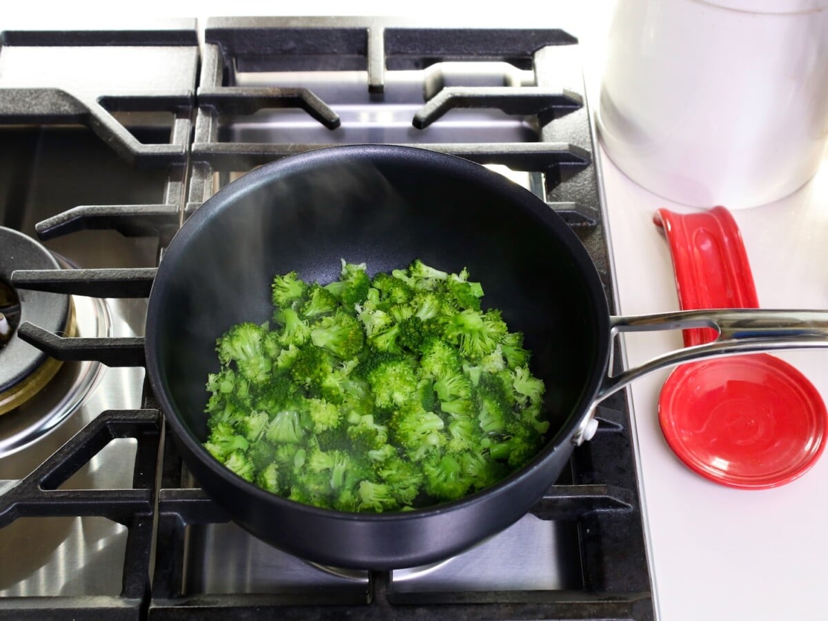 Steaming broccoli florets in a large pan over the top of cooking range.